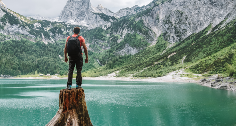 Wanderer auf einem Baumstumpf schaut auf klaren Bergsee