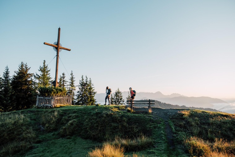 Zum Wandern bei Salzburg gehört St. Johann. Auf dem Bild sieht man Frauen vor einem Gipfelkreuz.