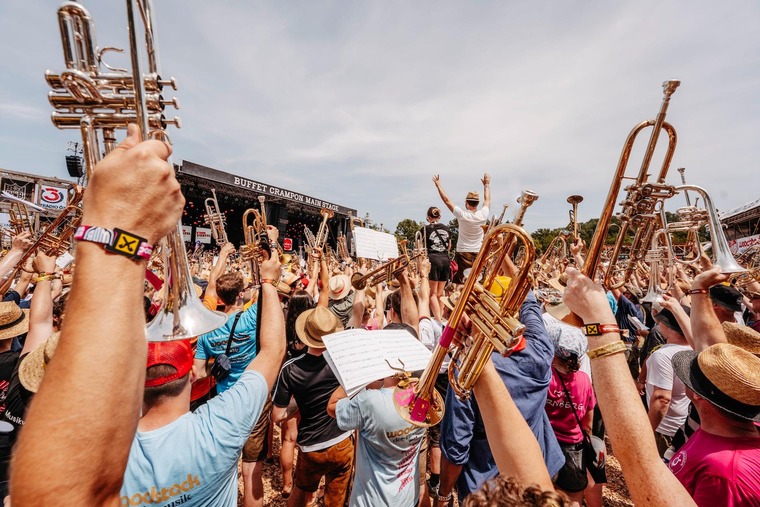 Die besten Festivals in Österreich: Das Woodstock der Blasmusik. Auf dem Bild sieht man viele Hände und Arme in einer Menschenmenge vor einer Festivalbühne – sie alle halten Blechinstrumente. 