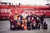 Eine Gruppe Mitarbeitende der ÖBB in verschiedenen Uniformen jubelnd und vor einem Zug stehend