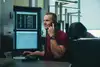Mann in roten T-Shirt vor Bildschirmen am Telefon.
