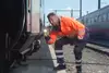 Mann in orangener Uniform untersucht Zugwaggon mit Taschenlampe.
