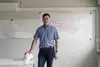 Mann mit kurzen Haaren und kariertem Hemd steht vor einem Bauplan.