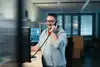 Mann mit Brille vor Bildschirmen stehend und am Telefon.