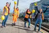 Menschengruppe mit Warnweste und gelben Schutzhelmen jubelnd. 