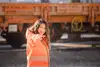 Eine Frau mit braunen Haaren und orangener Uniform zeigt in die Kamera. 