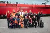 Eine Gruppe Mitarbeitende der ÖBB in verschiedenen Uniformen jubelnd und vor einem Zug stehend