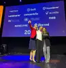 Drei ÖBB Mitarbeiterinnen stehen auf der Bühne und lachen in die Kamera. Eine Kollegin hält den Inspiring Workplace Award (ein schwarzer Quader auf dem in weißer Schrift „Inspire“ steht) in der Hand.