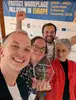 Foto aus der Selfie-Perspektive von vier ÖBB Mitarbeiter:innen, die lachend in die Kamera schauen. Eine Mitarbeiterin hält den EPBN WISE LGBTQIA+ Inclusion Award in die Kamera.