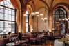 Essen in Wien: Ein Besuch im Café Central gehört einfach dazu. Im Bild sieht man den Gastraum des Cafés mit Gästen und Kellner:innen, die sitzen oder auch zwischen den Tischen gehen. 