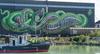 Linzer Sehenswürdigkeiten: Ein großes Mural auf einer Hausmauer im Linzer Hafen zeigt eine überdimensionale Schlange. Im Vordergrund ein Sightseeing-Schiff. 