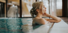 Wellness in Österreich: Eine Frau steht am Beckenrand und hat die Augen genüsslich geschlossen, hinter ihr hellblaues Wasser. 