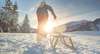 Eine Person zieht in einer schneebedeckten Landschaft einen Schlitten hinter sich her