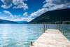 Blick auf den Ossiacher See bei Villach. Ein Steg ragt rechts in den See, am Horizont Berge. 