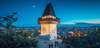 Graz Sehenswürdigkeiten: Blick auf den Grazer Uhrturm und die dahinterliegende Stadt bei Nacht. 