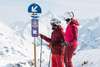 Mit dem Zug in den Skiurlaub: Zwei Skifahrer:innen blicken im Skigebiet Ski Arlberg auf einen Wegweiser zur legendären Runde "Run of Fame"