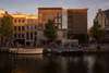 Zu den Sehenswürdigkeiten in Amsterdam zählt auf jeden Fall auch das Anne Frank Haus. Auf dem Bild sieht man das Haus von außen in der Abendsonne, der Blick von der anderen Seite einer Gracht. Davor liegen Boote im Wasser. 