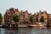 Zu den Sehenswürdigkeiten in Amsterdam gehört eine Grachtentour. Auf dem Bild zu sehen ist  Schiff mit Passagieren vor einem alten Gebäude.