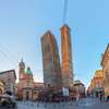 Zu den Bologna Sehenswürdigkeiten gehören die Garisenda- und Asinelli-Türme. Auf dem Bild sieht man sie von außen an einem sonnigen Tag, dahinter der blaue Himmel. 
