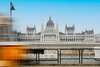 Budapest Sehenswürdgkeiten: Blick auf das Parlament in Budapest von der gegenüberliegenden Flussseite, davor sieht man unscharf eine Straßenbahn vorbei fahren. 