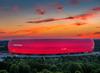 München Sehenswürdigkeiten: Blick auf die rot beleuchtete Allianz Arena von außen, aus der Vogelperspektive und in der roten Abenddämmerung. 
