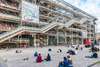 Zu den Sehenswürdigkeiten von Paris gehört das Centre Pompidou. Im Bild sieht man Menschen, die vor dem Gebäude auf den Stufen sitzen. 
