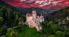 Wer mit dem Zug nach Rumänien fährt, sollte einen Stopp beim Schloss Bran in Brașov einlegen. Auf dem Bild sieht man das Dracula-Schloss Bran unter einem roten Abendhimmel. 
