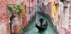 Venedig Sehenswürdigkeiten: Ein Gondolieri auf seiner Gondola in einem engen Kanal, gesäumt von bunten Häusern. 