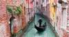 Venedig Sehenswürdigkeiten: Ein Gondolieri auf seiner Gondola in einem engen Kanal, gesäumt von bunten Häusern. 