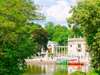 Zu den Warschau Sehenswürdigkeiten gehört der Łazienki-Park. Auf dem Bild zu sehen ist ein Teich, umgeben von viel Grün sowie königliche Gebäude. 