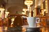 Prag Restaurant: Blick auf eine Kaffeetasse samt Untertasse, im Hintergrund ein klassisches Café. 