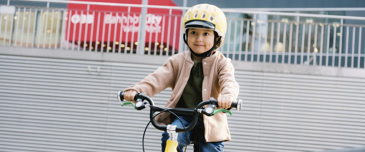 Kleines Kind fährt ein Fahrrad und trägt einen gelben Helm.