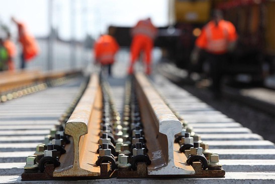 Nahaufnahme Schienen und Arbeiterinnen und Arbeitern auf einer Baustelle