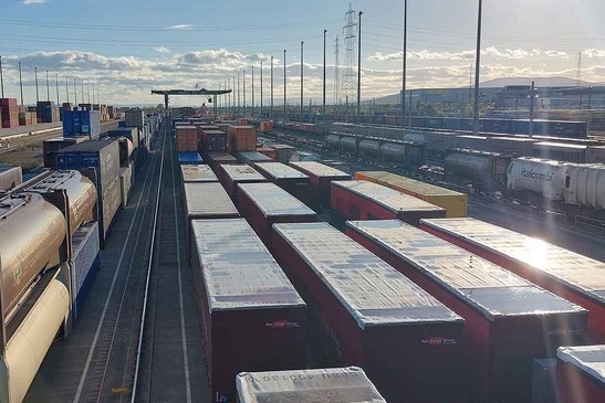Numerous loaded freight trains, a gantry crane can be seen in the background.