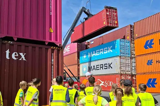 Viele Kinder mit Sicherheitswesten sehe zu, wie ein Stapler einen Container anhebt