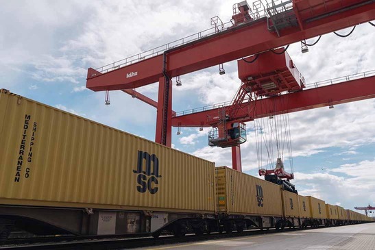 Train with yellow containers under a red gantry crane