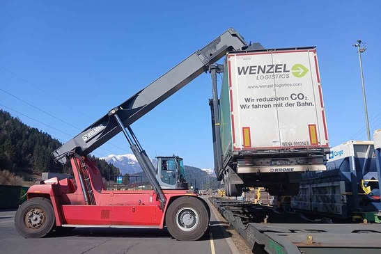 A reach stacker lifts a container onto a freight wagon.