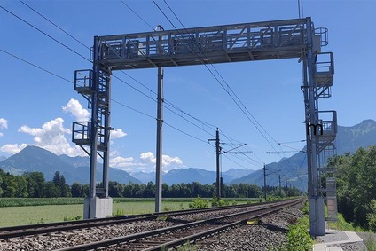 Train checkpoint above tracks with blue sky, meadow and mountains in the background