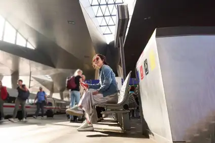 Frau sitzt am Bahnhof auf der Bank