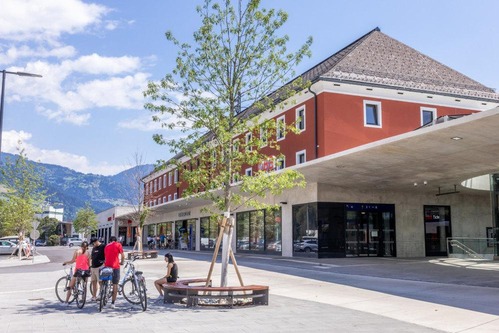 Photo: Lienz train station, forecourt with station building<br/>Text insert: Photo of station building and forecourt with cyclists in the foreground