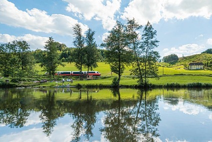 Zug fährt durch Hügellandschaft mit kleinem See