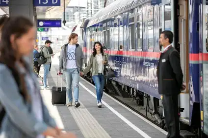 Zwei Personen gehen am Bahnsteig entlang, recht befindet sich der Nighjet.
