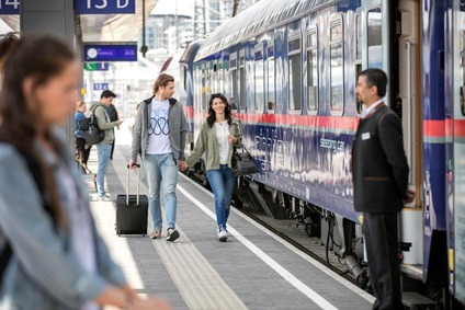 Zwei Personen gehen am Bahnsteig entlang, recht befindet sich der Nighjet.