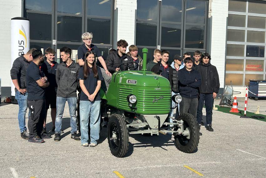 Lehrlinge stehen um einen grünen Traktor