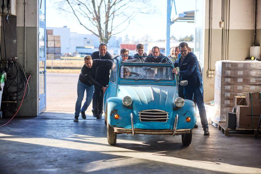 Lehrlinge und Ausbilder schieben Kultauto in die Werkstätte