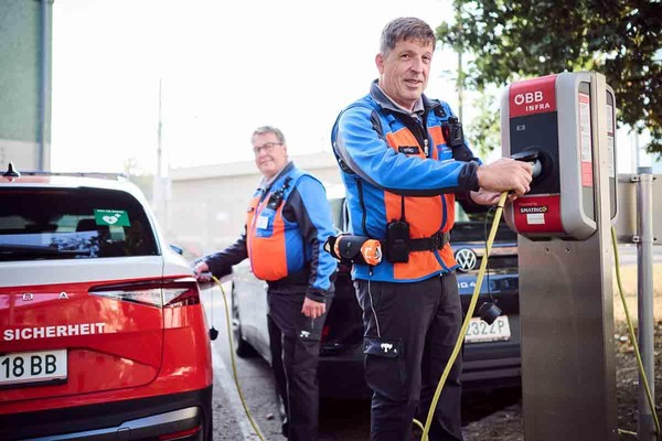 Zwei Sicherheitsmitarbeiter vor einem E-Auto an einer ÖBB-Elektroautotankstelle.