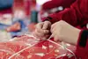 Hände, die ein weihnachtliches Päckchen einpacken. 