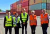 Fünf Personen in Warnwesten vor gestapelten Containern auf einem Güterterminal.