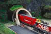 Rotes Schienenfahrzeug mit weißem Schriftzug hydrojet und weißem Schriftzug ÖBB von rechts kommend, in einen in einem Berg befindlichen Tunnel einfahrend