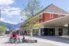 Foto Bahnhof Lienz, Vorplatz mit Bahnhofsgebäude<br/>Textinsert: Foto von Bahnhofsgebäude und Vorplatz und Radfahrern im Vordergrund